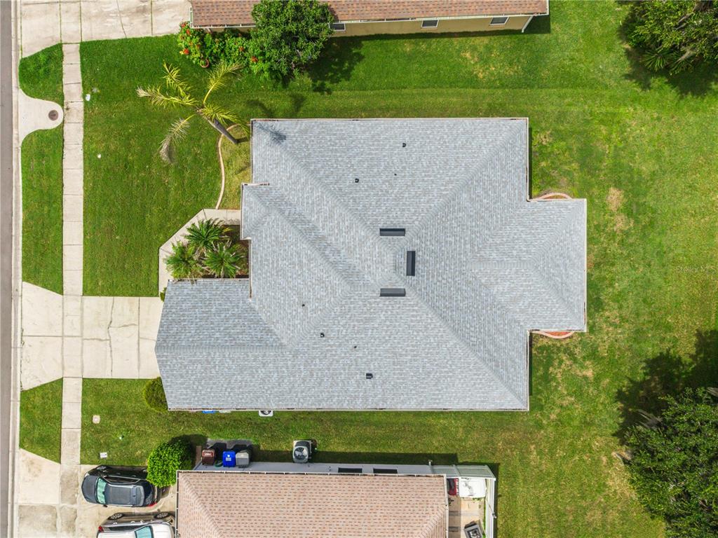 An aerial view shows the gray shingled roof of a house surrounded by a green lawn — 2106 THE OAKS BOULEVARD, KISSIMMEE, FL