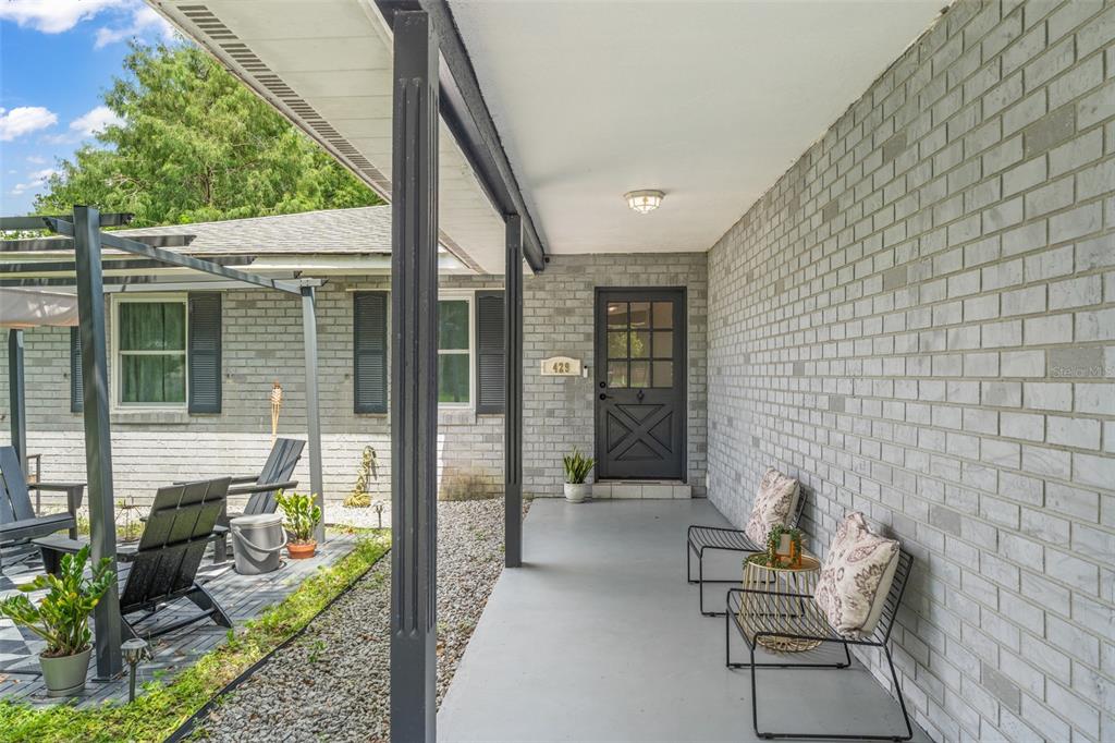 A covered front porch features gray brick walls, a dark door, and metal patio furniture — 429 VIRGINIA AVENUE, ST CLOUD, FL