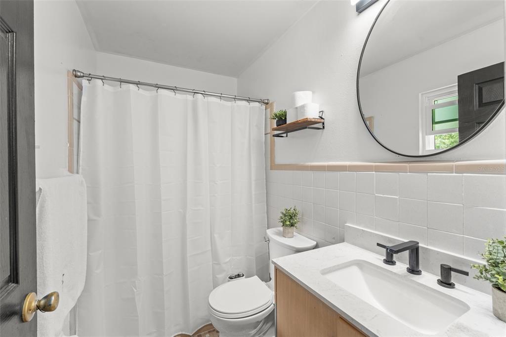 A bathroom features a white vanity, a round mirror, a toilet, and a shower curtain — 429 VIRGINIA AVENUE, ST CLOUD, FL