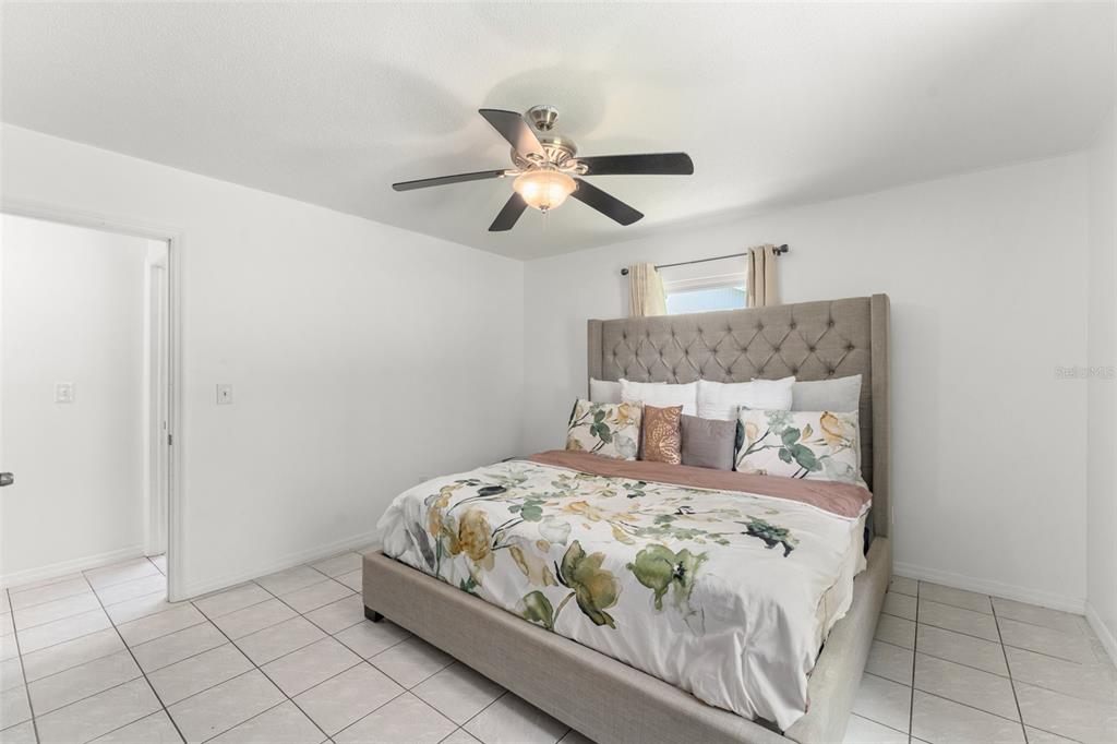 A bedroom features a tufted upholstered bed, white walls, and light-colored tile flooring — 429 VIRGINIA AVENUE, ST CLOUD, FL