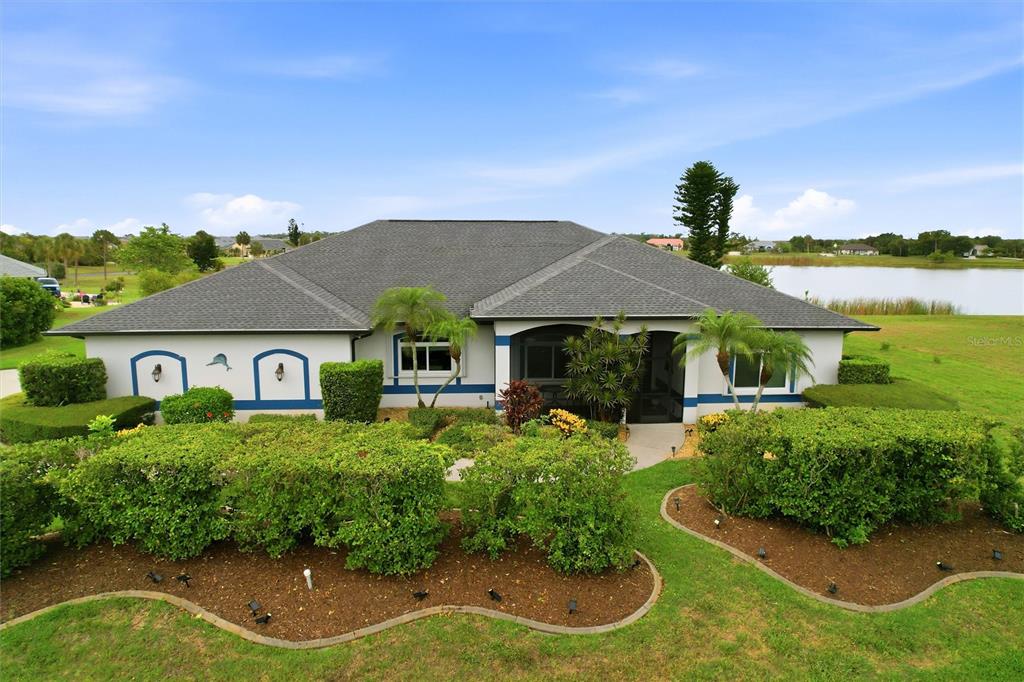 A single-story house with a gray roof and white exterior sits beside a lake — 7100 SAN CASA DRIVE, ENGLEWOOD, FL