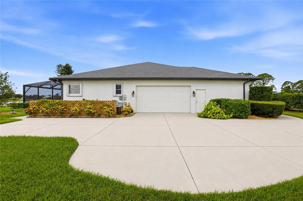 A white house exterior features a two-car garage, a concrete driveway, and landscaped bushes — 7100 SAN CASA DRIVE, ENGLEWOOD, FL