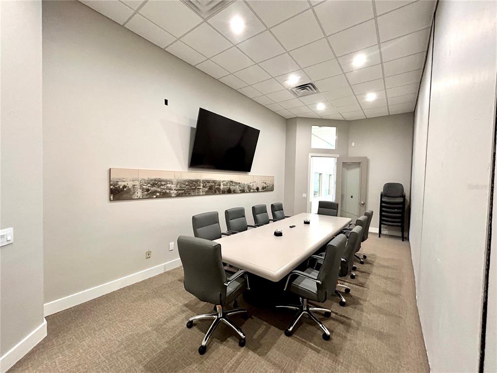 A conference room features a long table, gray chairs, a wall-mounted television, and carpeted flooring — 1203 W MARION AVENUE, PUNTA GORDA, FL