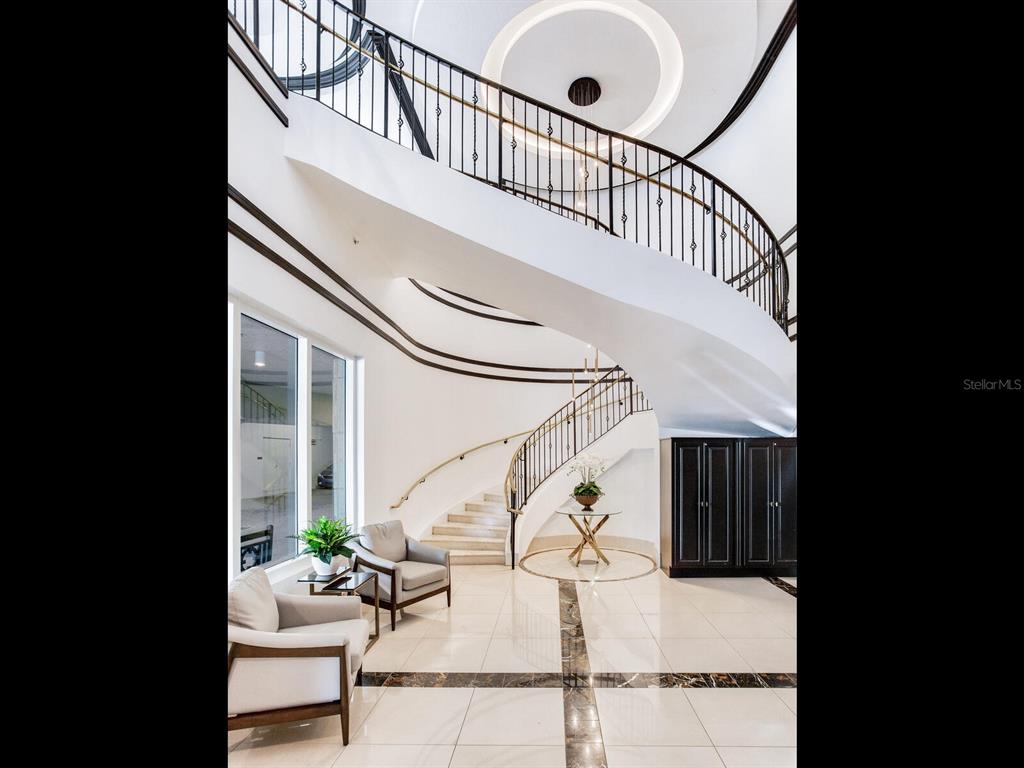 A grand foyer features a curved staircase, tiled floors, and two armchairs near a window — 3507 BAYSHORE BOULEVARD UNIT 2001, TAMPA, FL