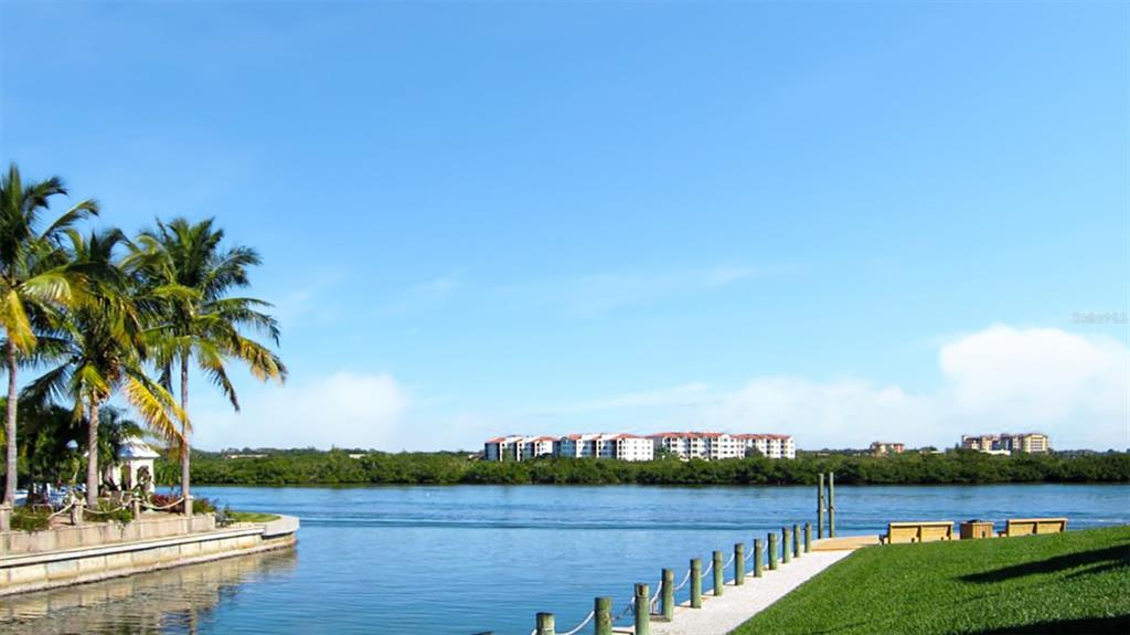 A view of a waterfront area with palm trees, a dock, and distant apartment buildings — 1351 SIESTA BAYSIDE DRIVE UNIT 1351-D, SARASOTA, FL