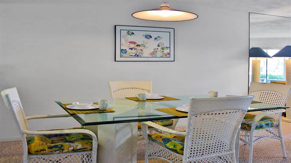 A dining room features a glass-topped table, wicker chairs with patterned cushions, and wall art — 1351 SIESTA BAYSIDE DRIVE UNIT 1351-D, SARASOTA, FL