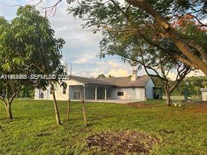 A single-story house with a covered patio sits on a grassy lot with large trees — 15854 Tangelo Blvd, Loxahatchee FL 33412, LOXAHATCHEE, FL