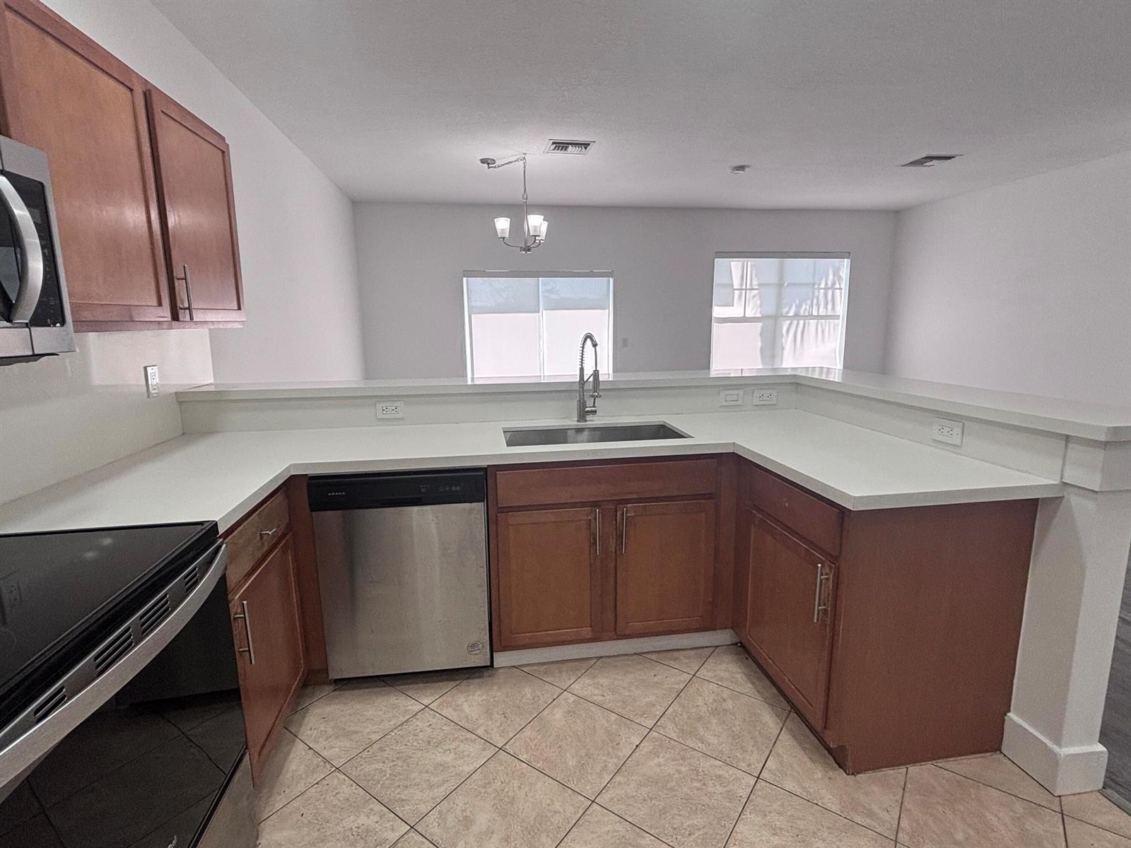 A kitchen features wood cabinets, white countertops, stainless steel appliances, and tile flooring — 3904 Sabal Way, Fort Pierce FL 34981, FORT PIERCE, FL