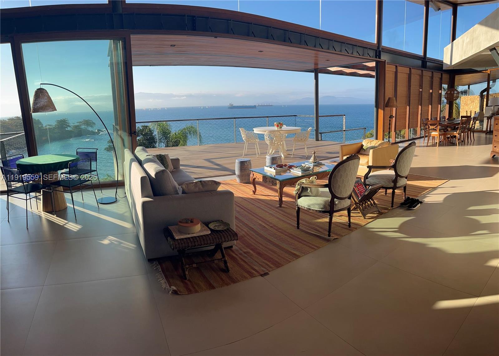 A spacious living room opens to a large deck overlooking the ocean and distant mountains — 8557 Av. Eng. Martinho Storace, 00000, FL