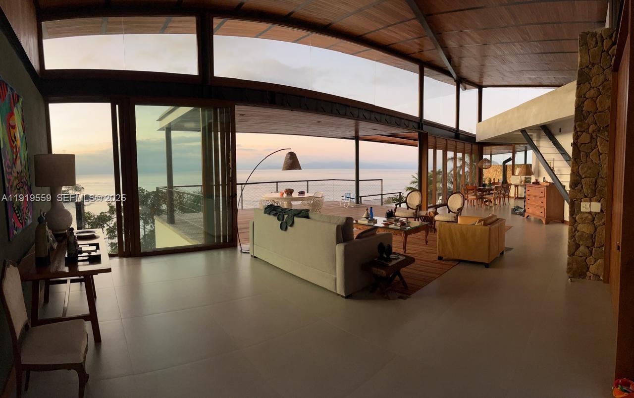 A spacious open-concept living room features floor-to-ceiling glass walls overlooking a sunset ocean view — 8557 Av. Eng. Martinho Storace, 00000, FL