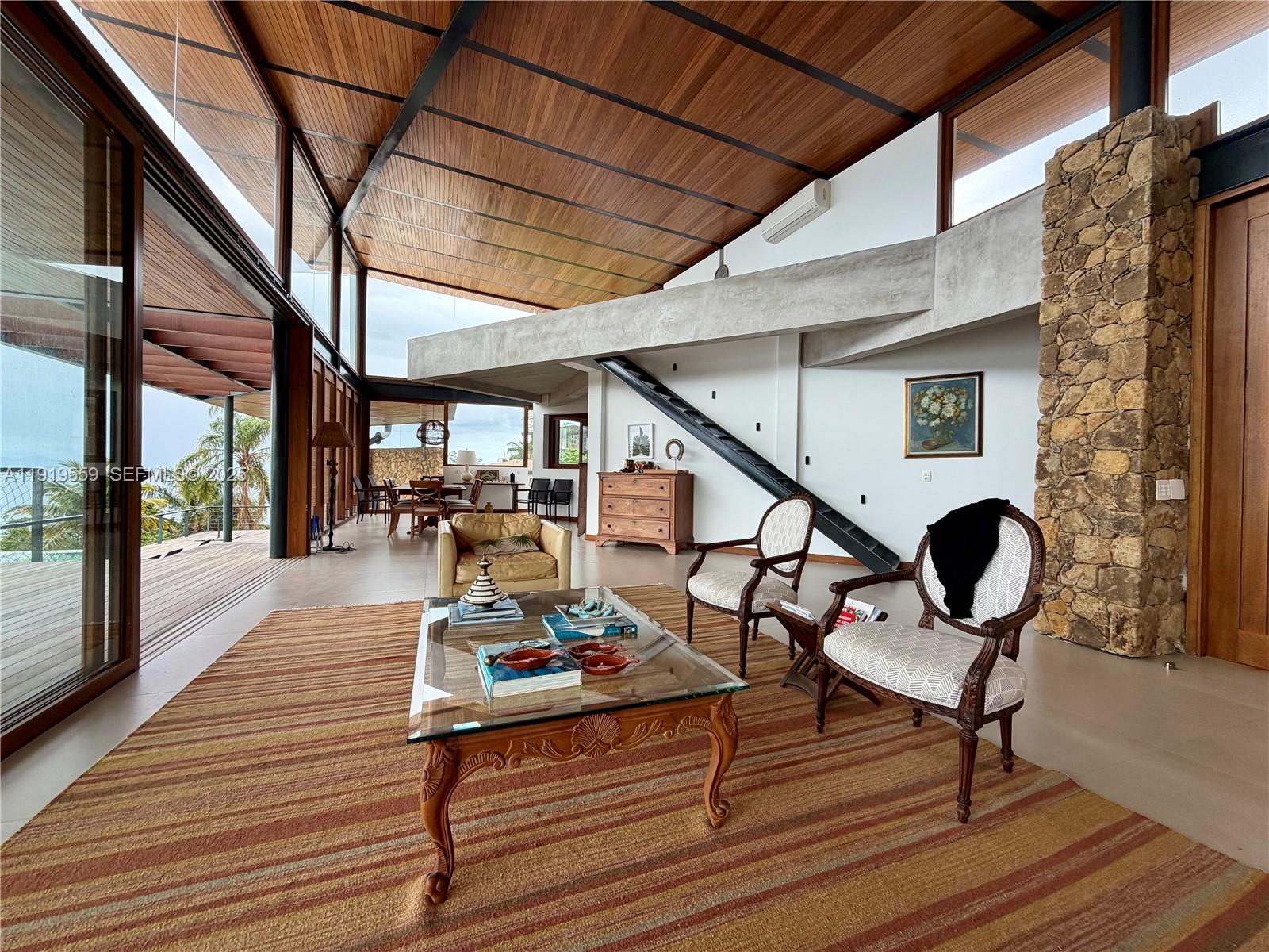 A spacious living room features a vaulted wood ceiling, stone pillar, and glass walls — 8557 Av. Eng. Martinho Storace, 00000, FL