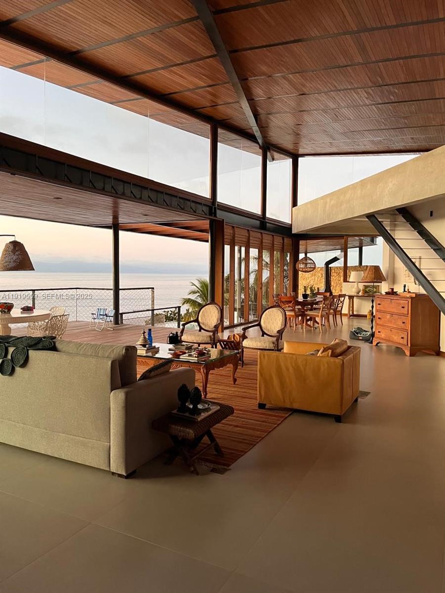 A spacious open-concept living area features wood ceilings, large glass walls, and ocean views — 8557 Av. Eng. Martinho Storace, 00000, FL