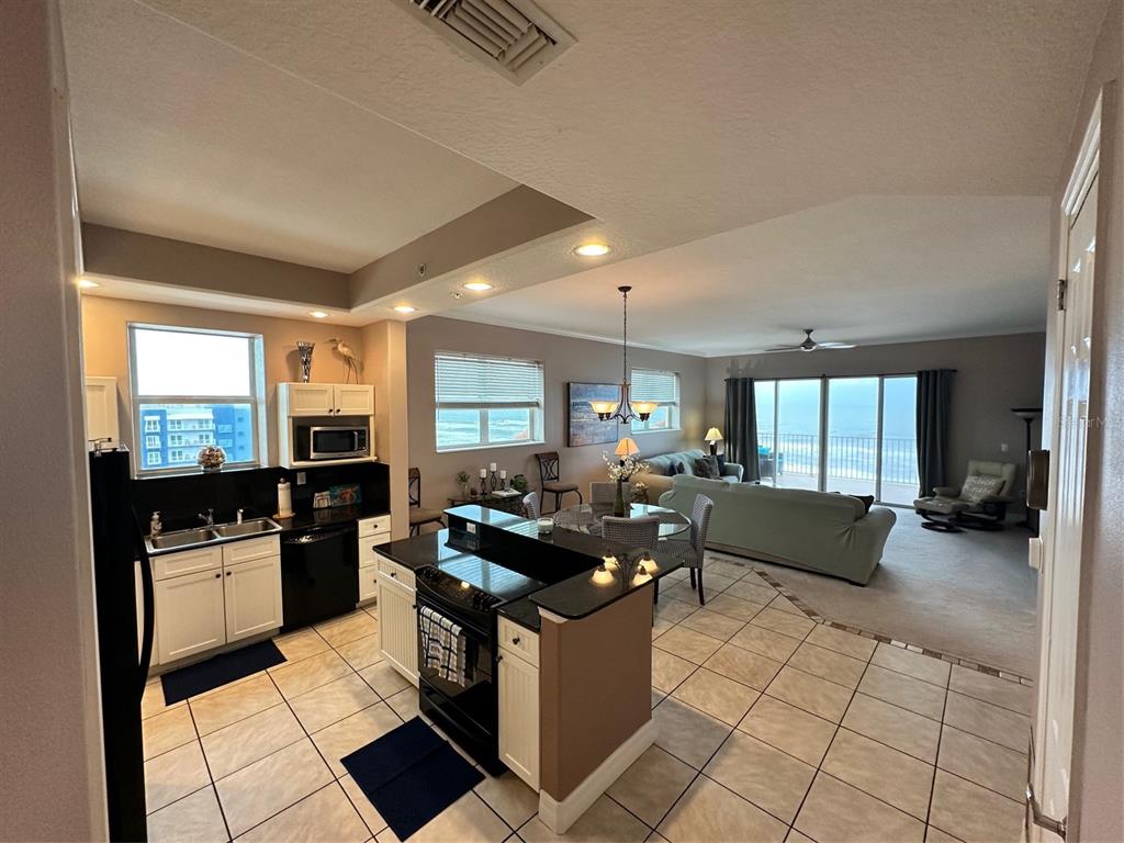 An open-concept kitchen with white cabinets and black appliances overlooks a living area with ocean views — 711 S ATLANTIC AVENUE UNIT 701, NEW SMYRNA BEACH, FL