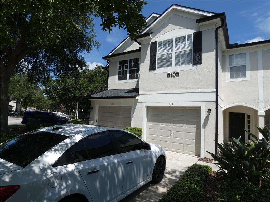 A two-story residential building features beige stucco walls, two garage doors, and a white car parked in front — 6105 TWAIN STREET UNIT 102, ORLANDO, FL