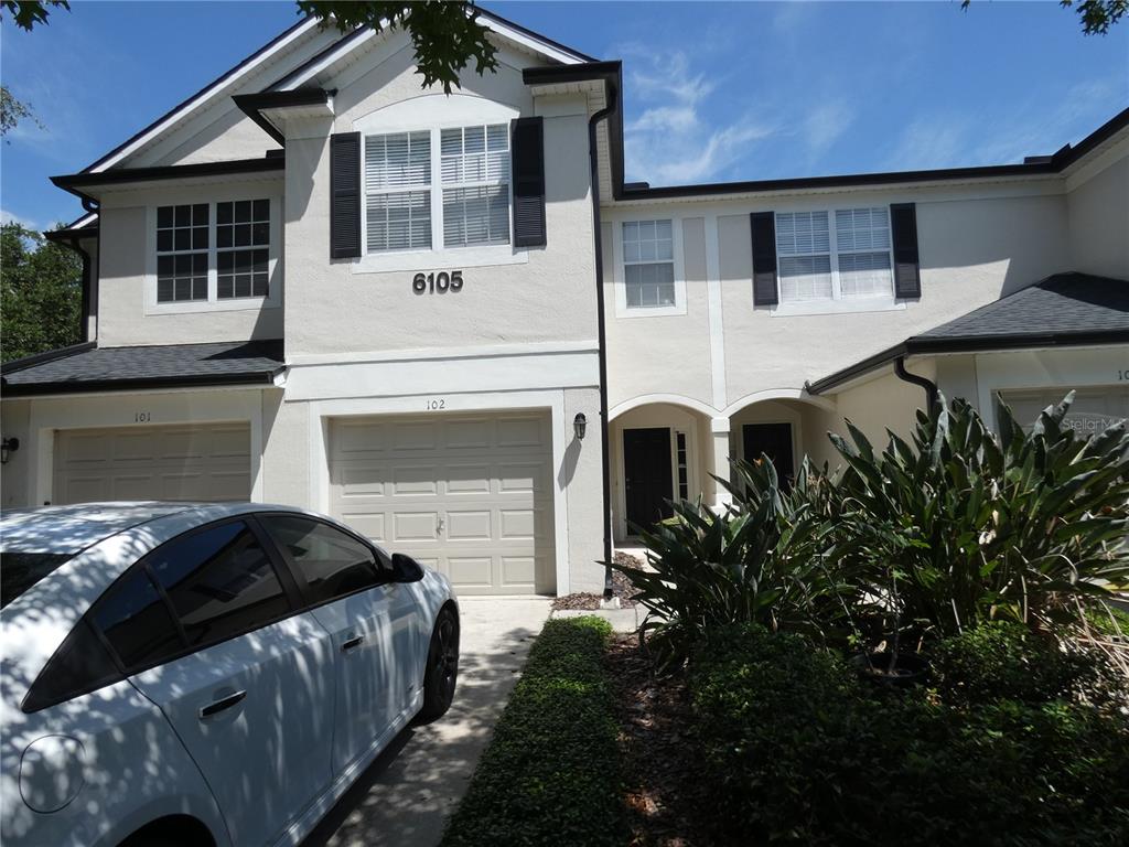 A two-story townhouse exterior features a beige stucco facade, black shutters, and two garage doors — 6105 TWAIN STREET UNIT 102, ORLANDO, FL