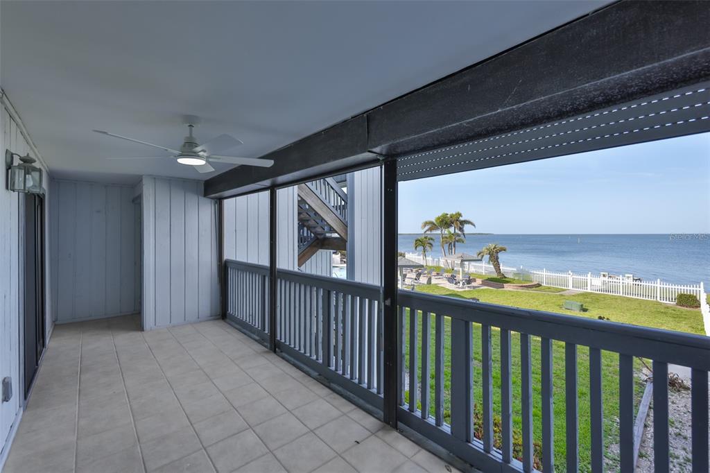 A covered balcony with a ceiling fan overlooks a lawn, white fence, and the ocean — 812 BAHIA DEL SOL DRIVE UNIT A, RUSKIN, FL