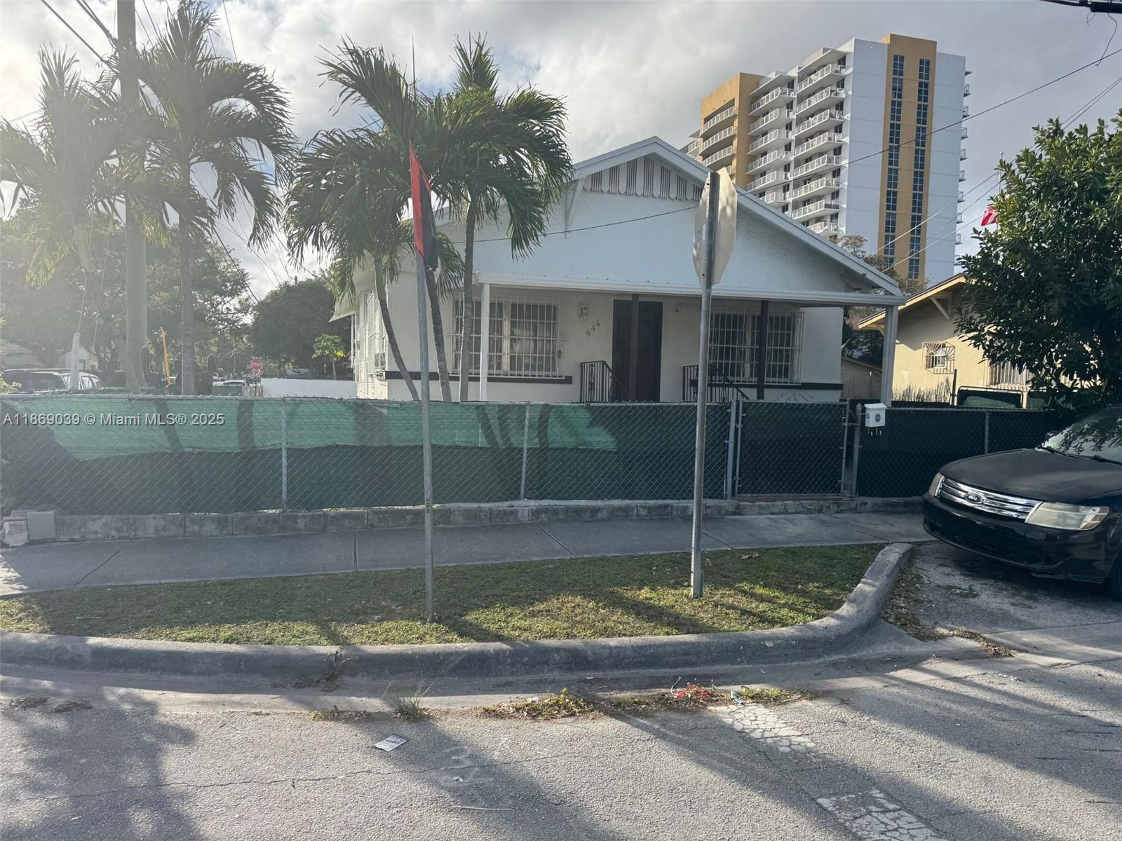 A white single-story house sits behind a chain-link fence with palm trees in the yard — 844 SW 8th Ct, Miami FL 33130, MIAMI, FL