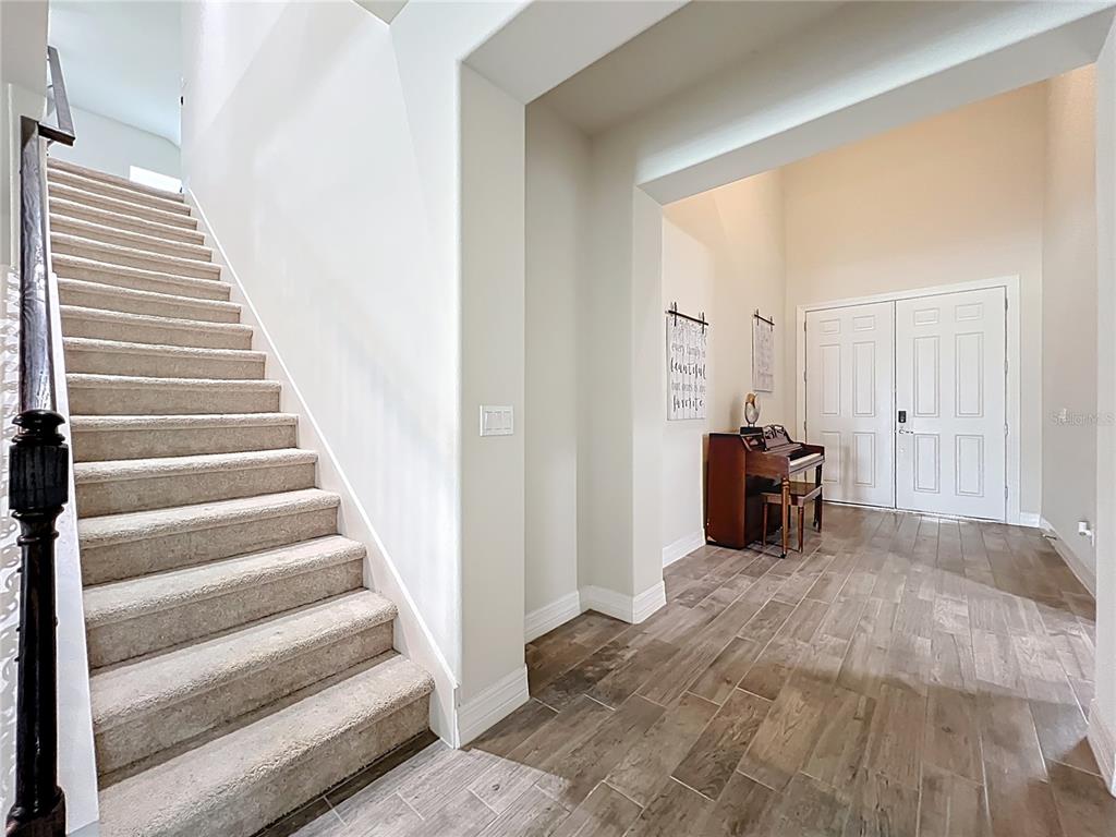 An entryway features a carpeted staircase, wood-look tile flooring, and a piano near the front door — 15084 CUDDY COURT, ORLANDO, FL