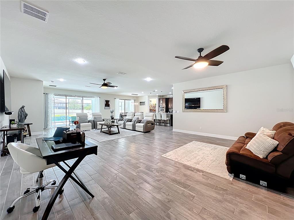 An open-concept living area features tile flooring, a desk, a brown sofa, and a kitchen — 15084 CUDDY COURT, ORLANDO, FL