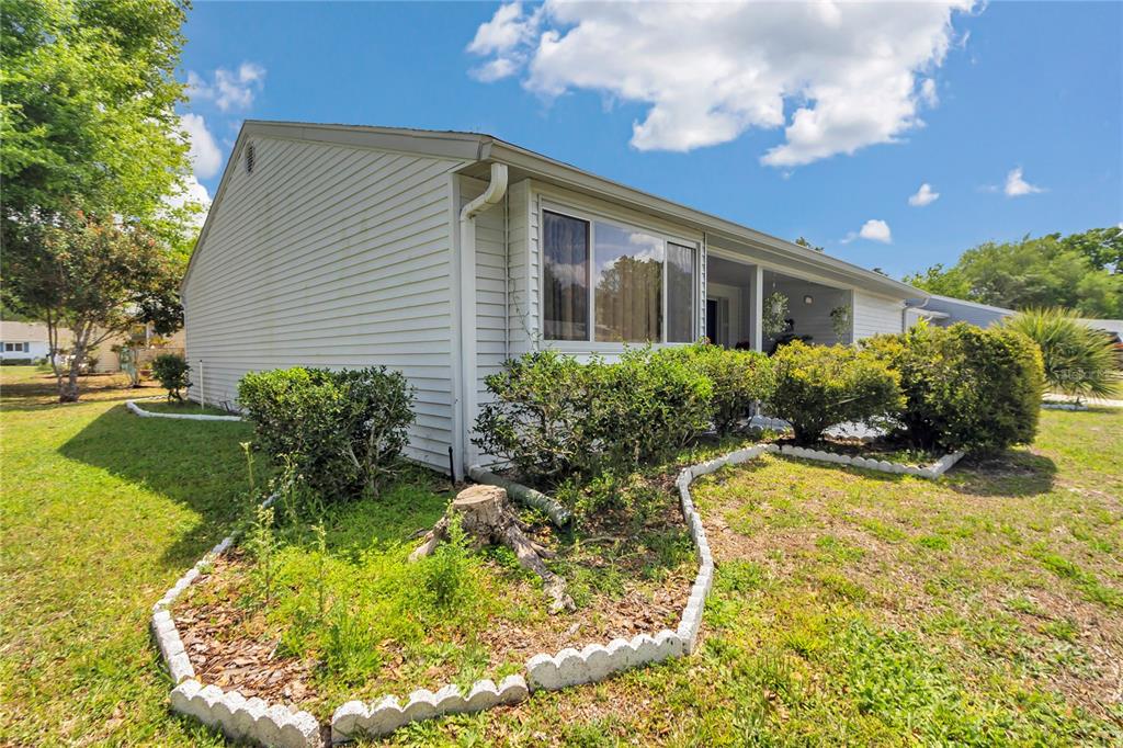 The exterior of a light-colored, single-story house features a screened porch and landscaped garden beds — 10841 SW 90TH COURT, OCALA, FL