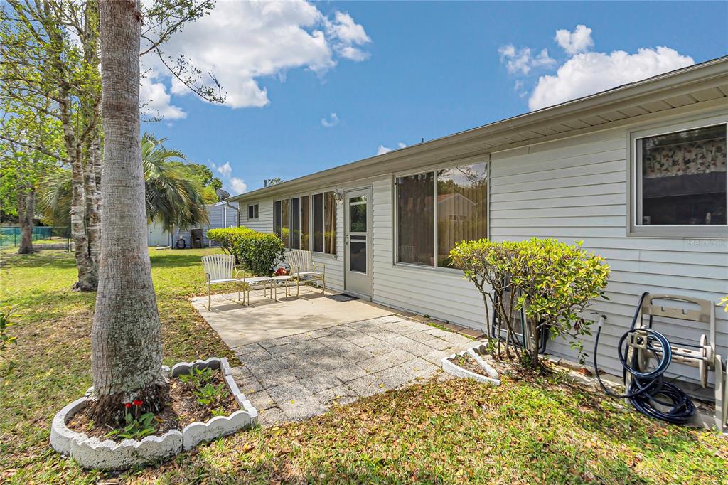 A backyard view of a house exterior featuring a stone patio, siding, and a palm tree — 10841 SW 90TH COURT, OCALA, FL
