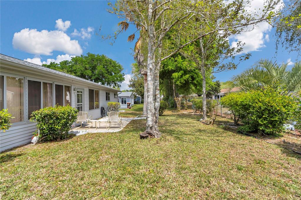 A backyard view of a single-story house with a small patio and mature trees — 10841 SW 90TH COURT, OCALA, FL