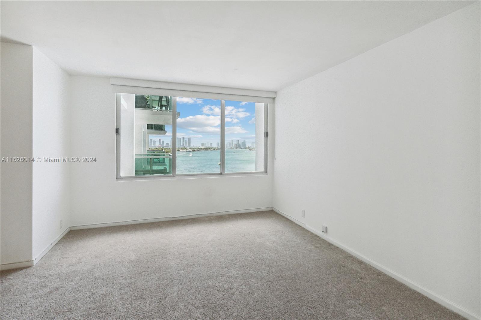 An empty room with beige carpet, white walls, and a window overlooking the water — 1000 West Ave # 821, Miami Beach FL 33139, MIAMI BEACH, FL