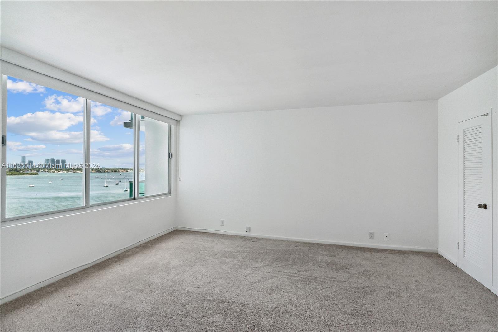 An empty room with beige carpet, white walls, a louvered closet door, and a water view — 1000 West Ave # 821, Miami Beach FL 33139, MIAMI BEACH, FL