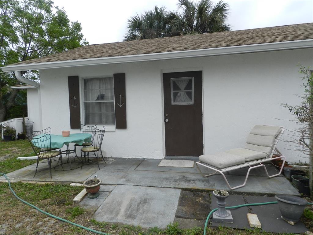 A white exterior wall features a brown door, a window with shutters, and a patio — 805 OCEAN AVENUE, NEW SMYRNA BEACH, FL