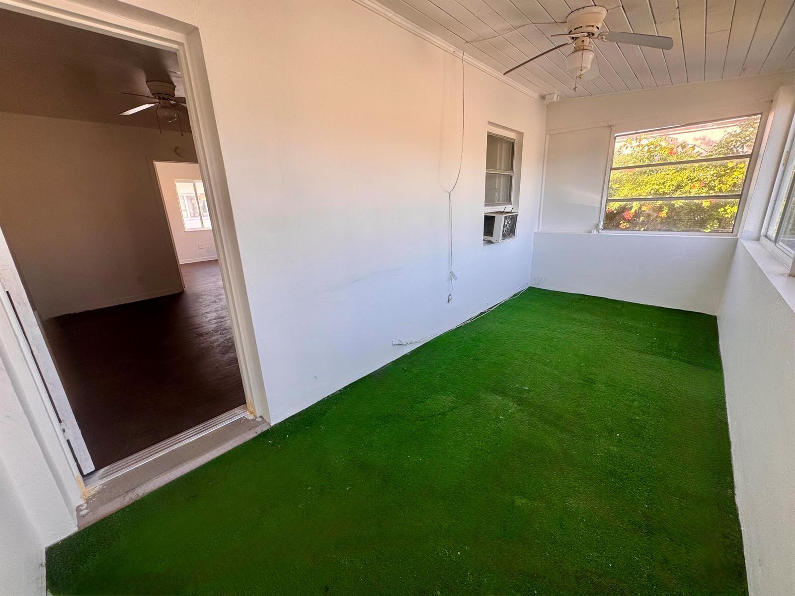 A sunroom with green artificial turf flooring, a ceiling fan, and a window air conditioner — 2515 Avenue E, Riviera Beach FL 33404, RIVIERA BEACH, FL