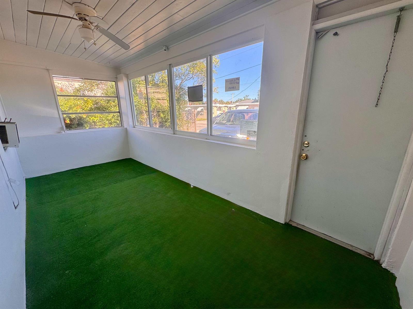A sunroom with white walls, a ceiling fan, and green artificial turf flooring — 2515 Avenue E, Riviera Beach FL 33404, RIVIERA BEACH, FL