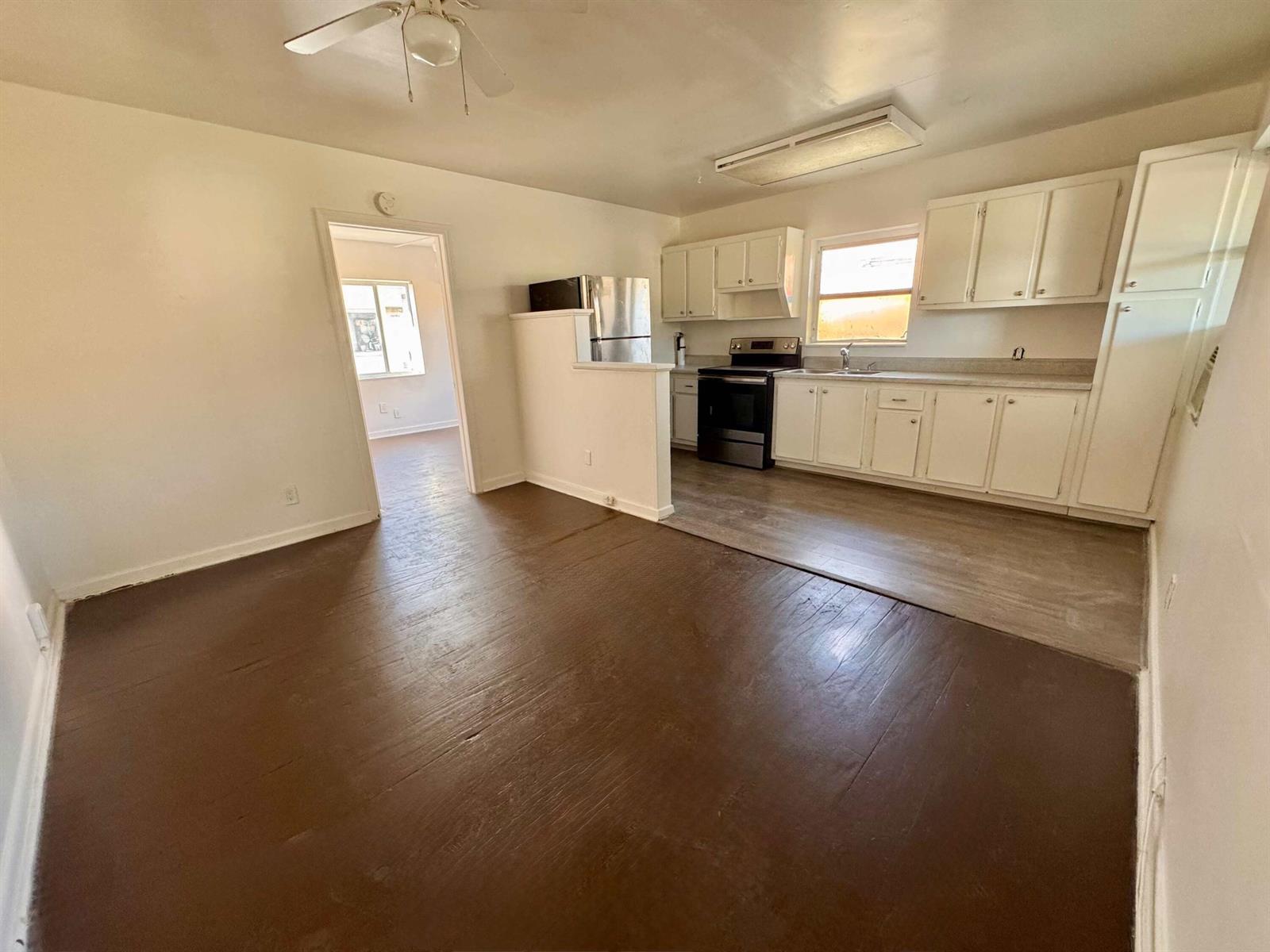 A kitchen with white cabinets and a dark wood floor opens into a living area — 2515 Avenue E, Riviera Beach FL 33404, RIVIERA BEACH, FL
