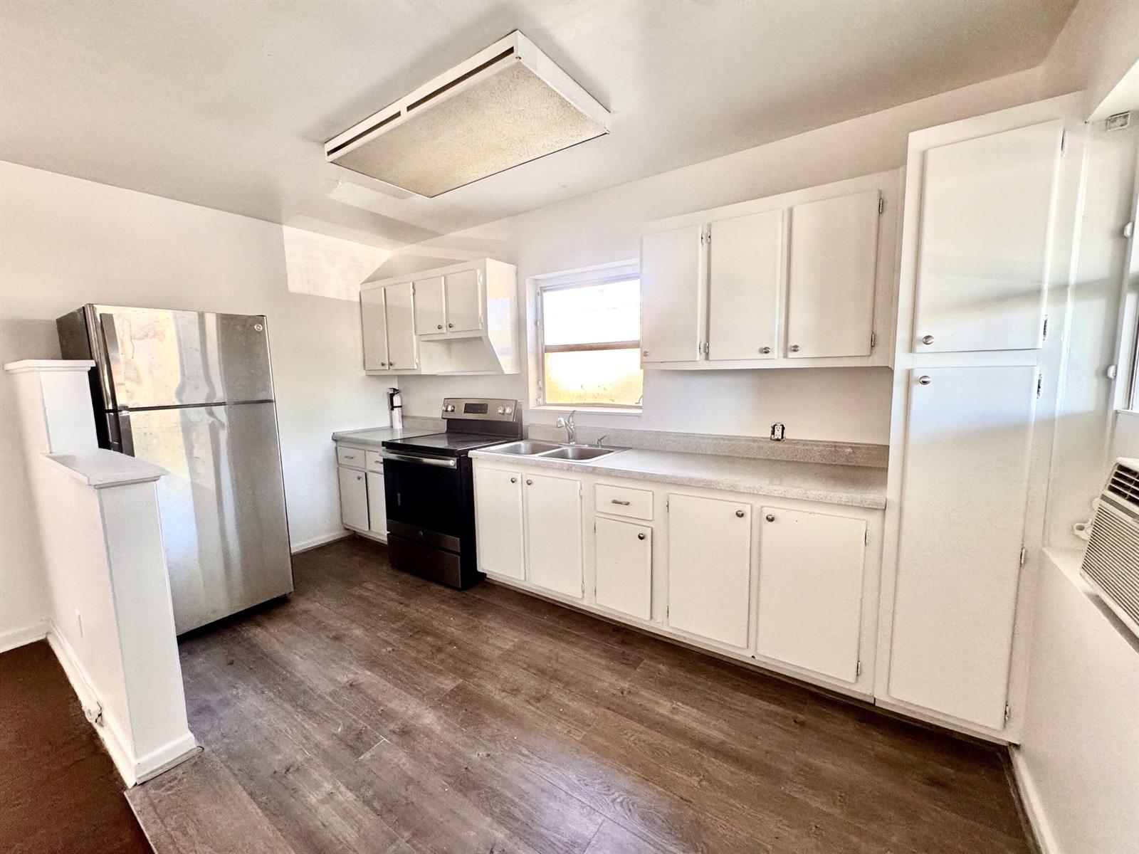 A kitchen features white cabinets, stainless steel appliances, a window, and wood-look flooring — 2515 Avenue E, Riviera Beach FL 33404, RIVIERA BEACH, FL