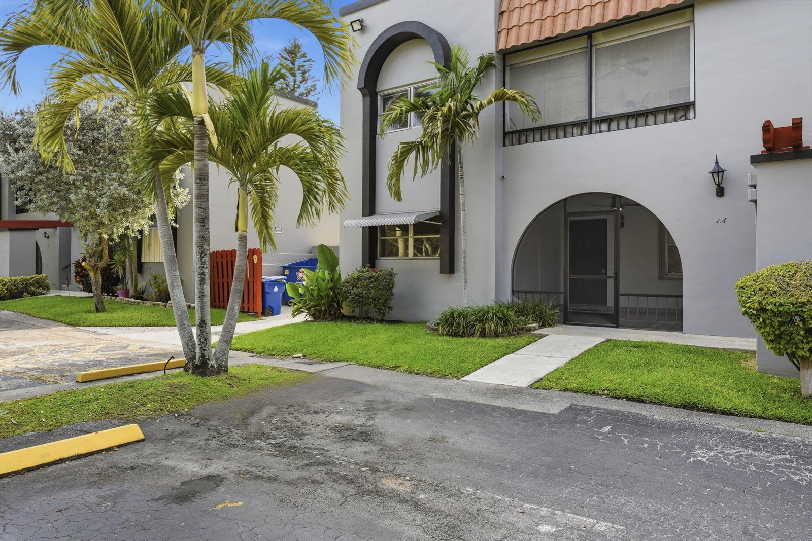 A two-story gray building features arched entryways, palm trees, and a paved parking area — 3851 NW 84th Avenue # 1a, Sunrise FL 33351, SUNRISE, FL