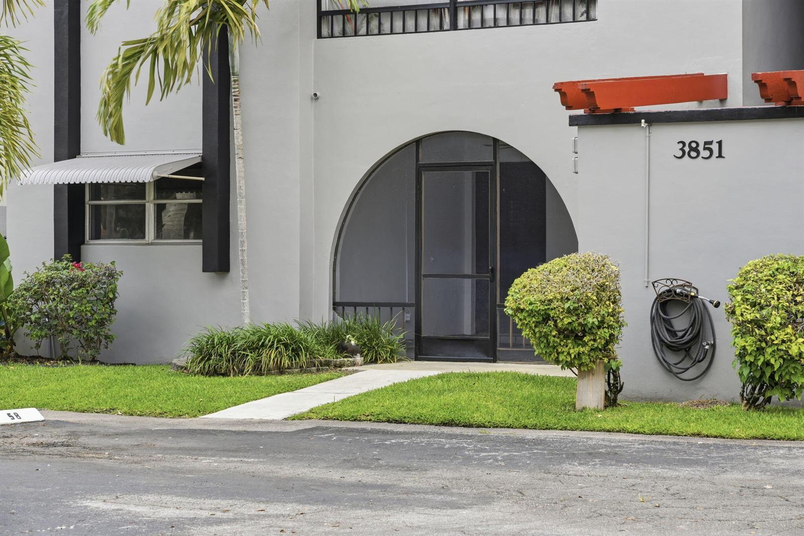 The exterior of a gray building features an arched entryway and a black screen door — 3851 NW 84th Avenue # 1a, Sunrise FL 33351, SUNRISE, FL
