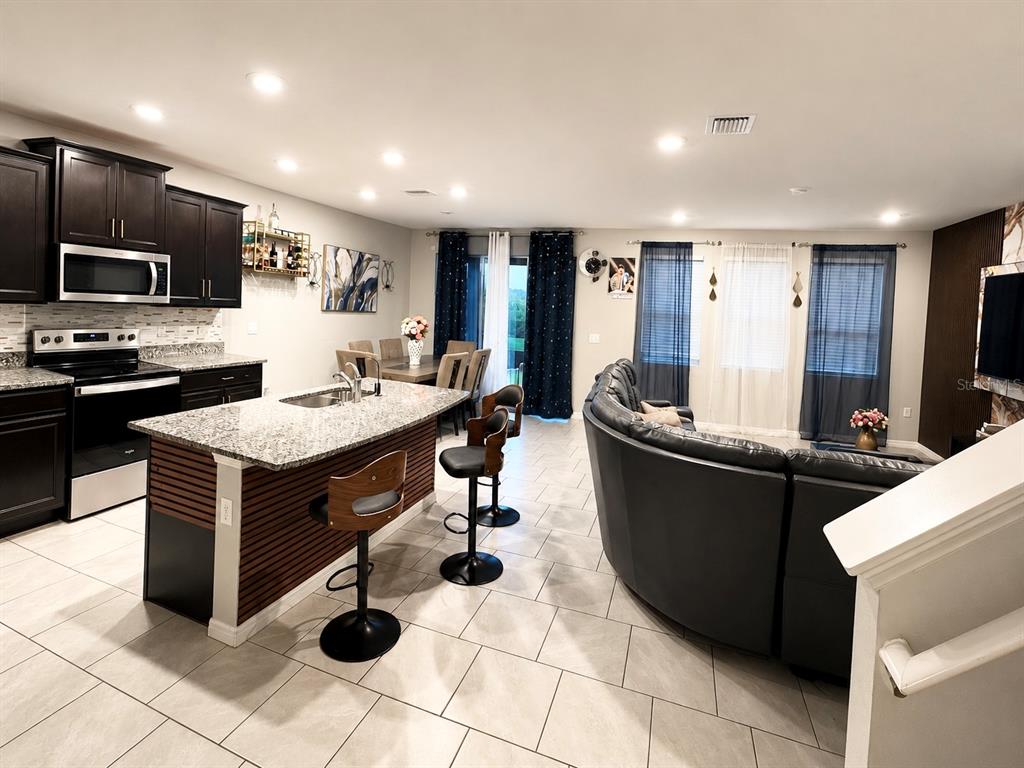 An open-concept kitchen with a granite island and dark cabinets overlooks a living room area — 3817 SUNNY SPRING STREET, PLANT CITY, FL