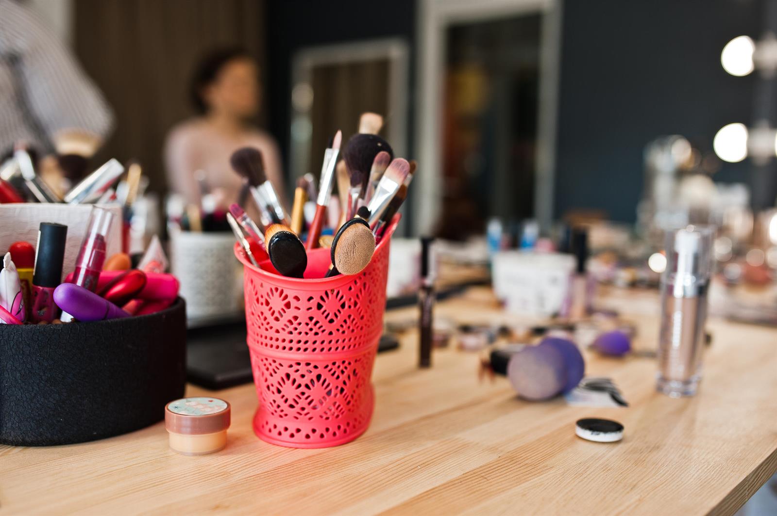 A wooden table holds a pink container filled with various makeup brushes and cosmetic products — Salon Midtown Miami Salon Midtown Miami, Miami FL, MIAMI, FL