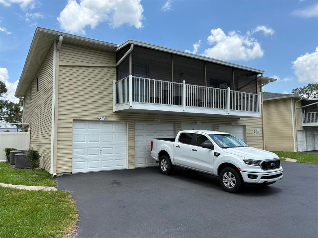 A two-story building with tan siding, a screened-in balcony, and a white pickup truck parked outside — 4361 SHADOW CREST PLACE UNIT 32-3, ORLANDO, FL
