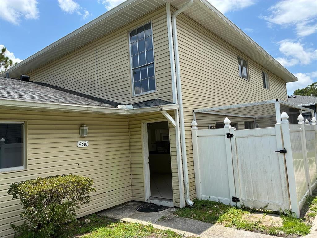 The exterior of a two-story house features beige vinyl siding, a white fence, and an entryway — 4361 SHADOW CREST PLACE UNIT 32-3, ORLANDO, FL