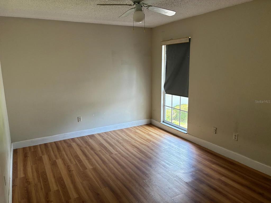An empty bedroom features wood-look flooring, beige walls, a ceiling fan, and a single window — 4361 SHADOW CREST PLACE UNIT 32-3, ORLANDO, FL