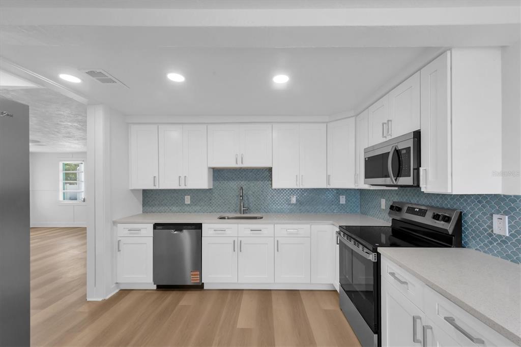 A kitchen with white cabinets, stainless steel appliances, and a blue scalloped tile backsplash — 358 BOCA CIEGA DRIVE, MADEIRA BEACH, FL