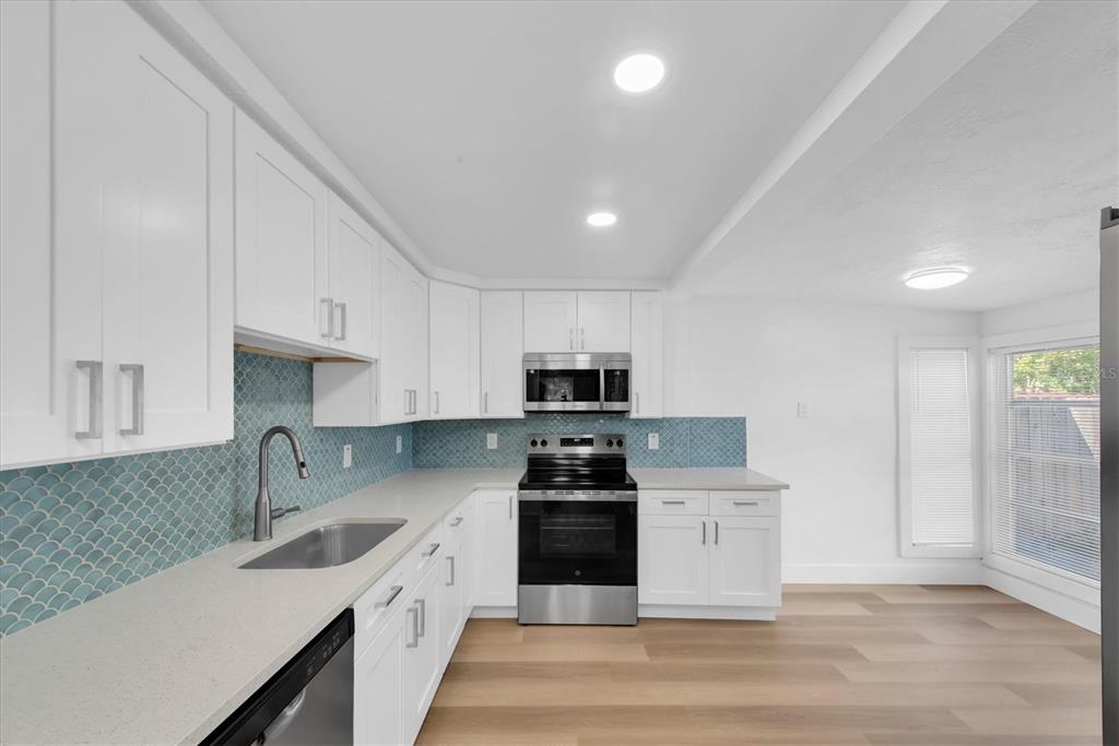 A kitchen features white cabinets, light countertops, a blue fish-scale backsplash, and stainless steel appliances — 358 BOCA CIEGA DRIVE, MADEIRA BEACH, FL
