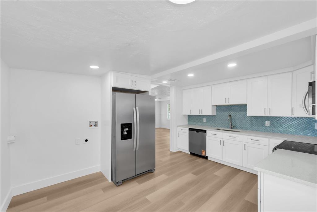 A modern kitchen features white cabinets, stainless steel appliances, and a blue tiled backsplash — 358 BOCA CIEGA DRIVE, MADEIRA BEACH, FL