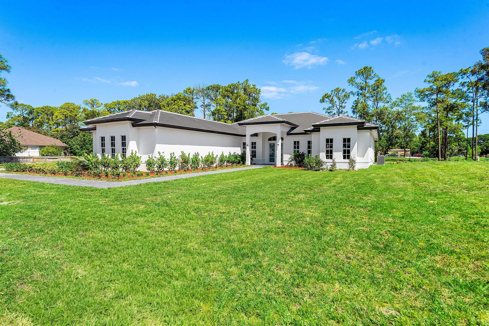 A white, single-story house with a dark tiled roof sits on a large grassy lot — 15090 Temple Boulevard, FL 33470, FL