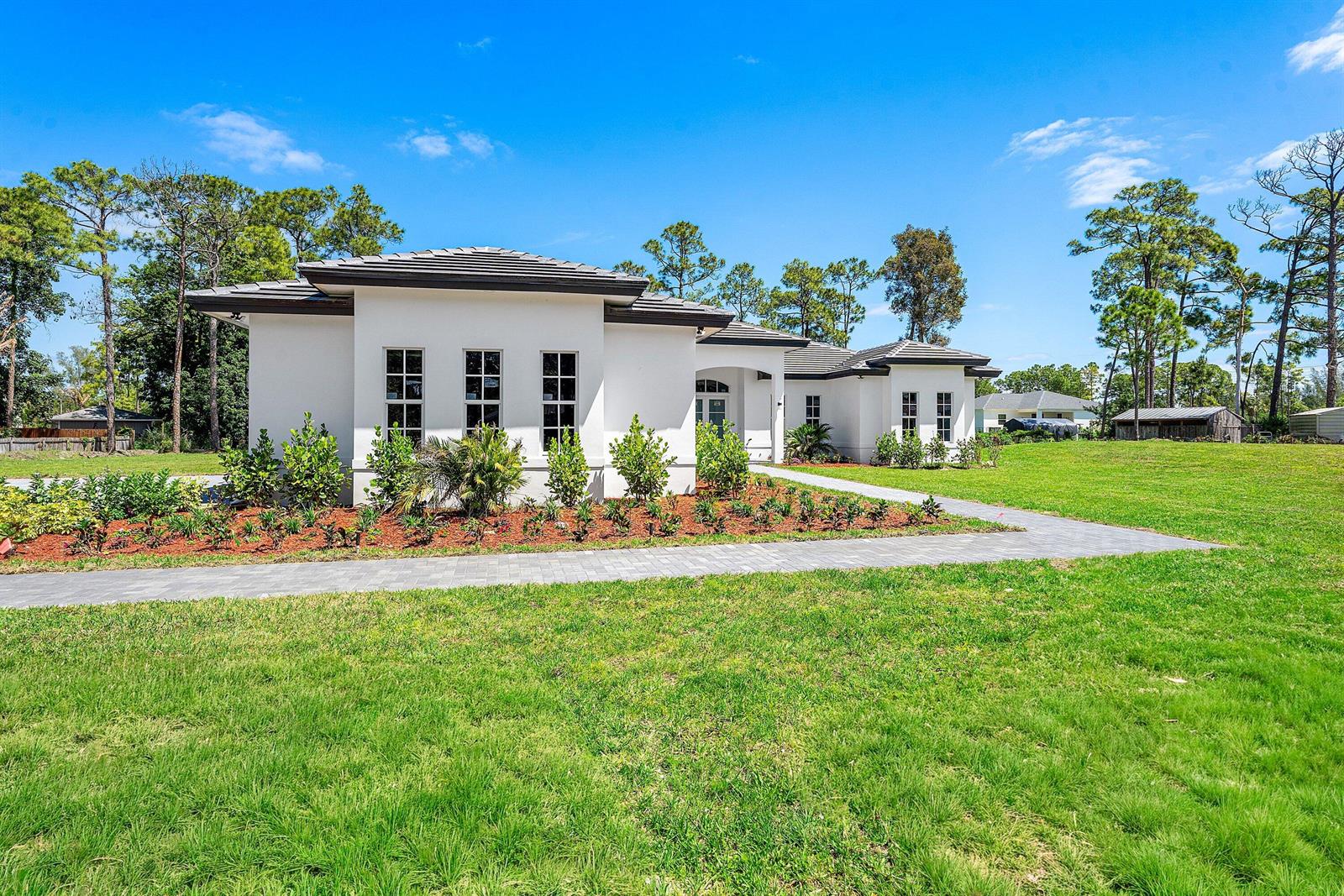 A modern white single-story house with a gray tile roof and a paved walkway — 15090 Temple Boulevard, FL 33470, FL