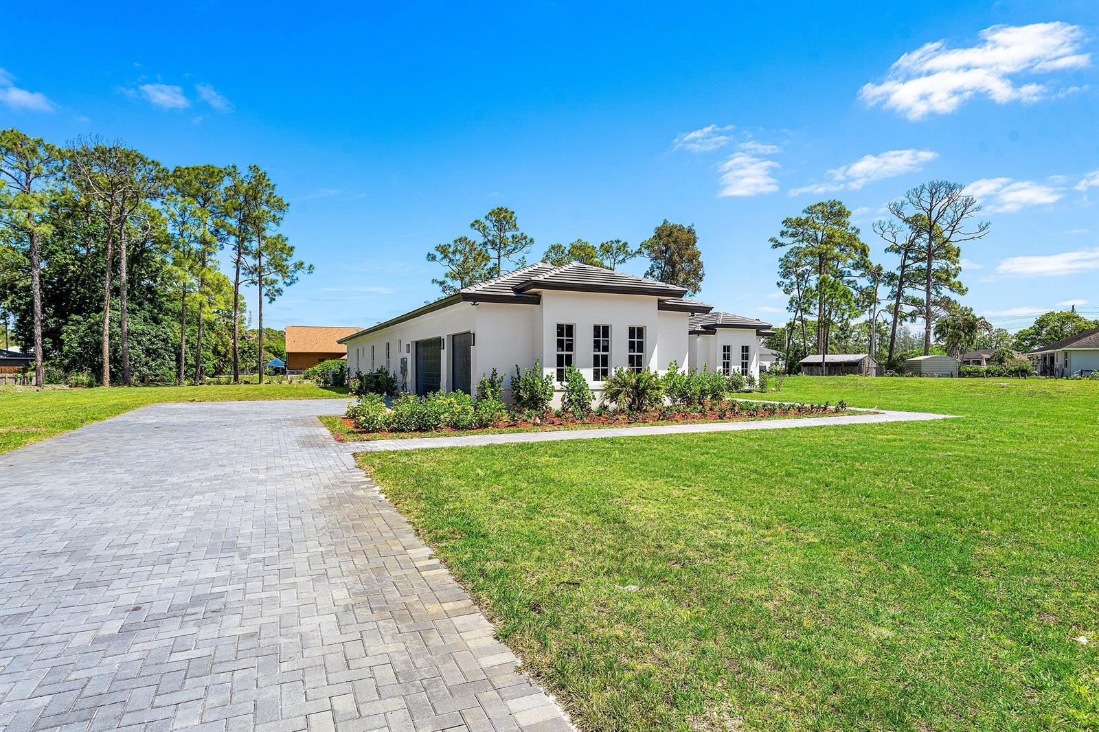 A modern white house with a gray tile roof and a paved driveway — 15090 Temple Boulevard, FL 33470, FL