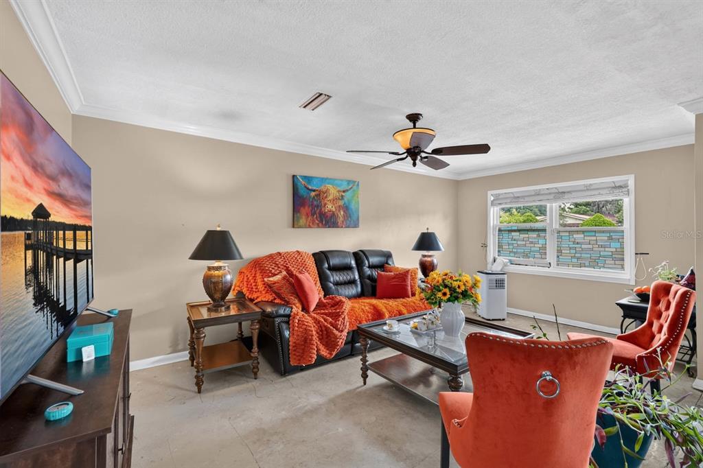 A living room features a black leather sofa, orange accents, a ceiling fan, and windows — 212 MIMOSA DRIVE, PALATKA, FL