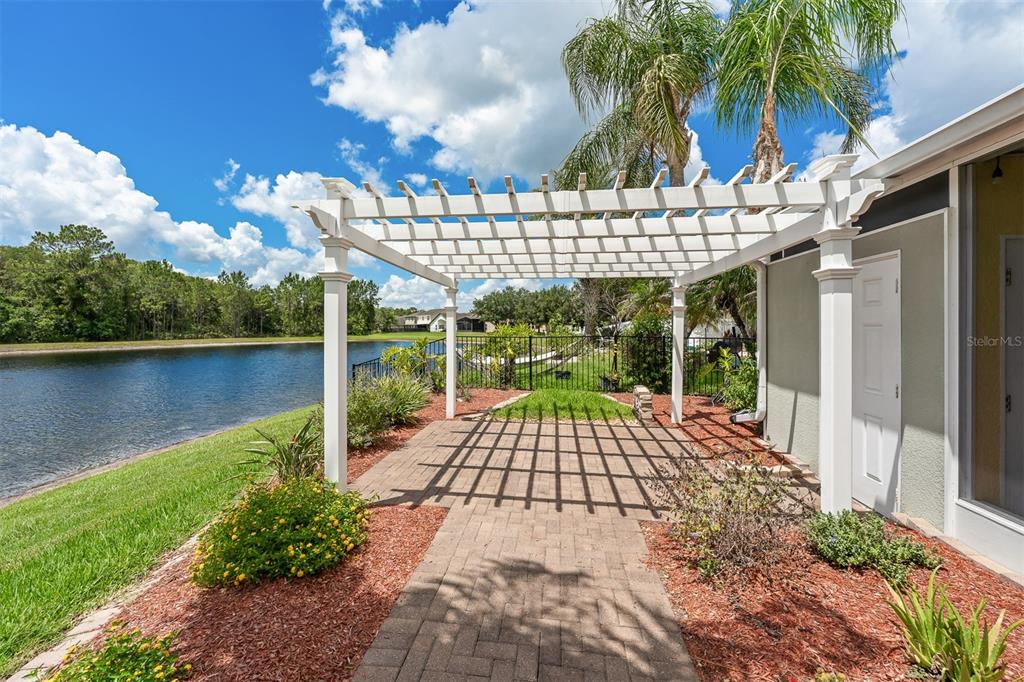 A white pergola stands over a brick patio next to a house overlooking a lake — 1465 BALSAM WILLOW TRAIL, ORLANDO, FL