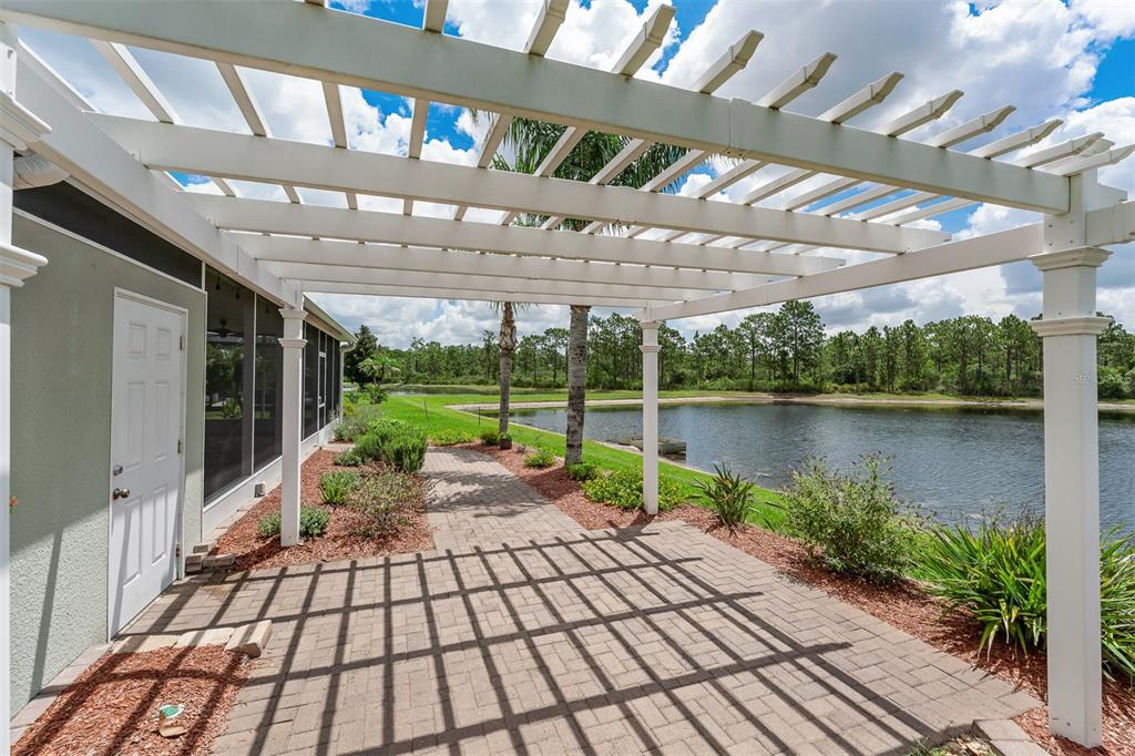 A white pergola covers a paved patio overlooking a lake behind a house — 1465 BALSAM WILLOW TRAIL, ORLANDO, FL