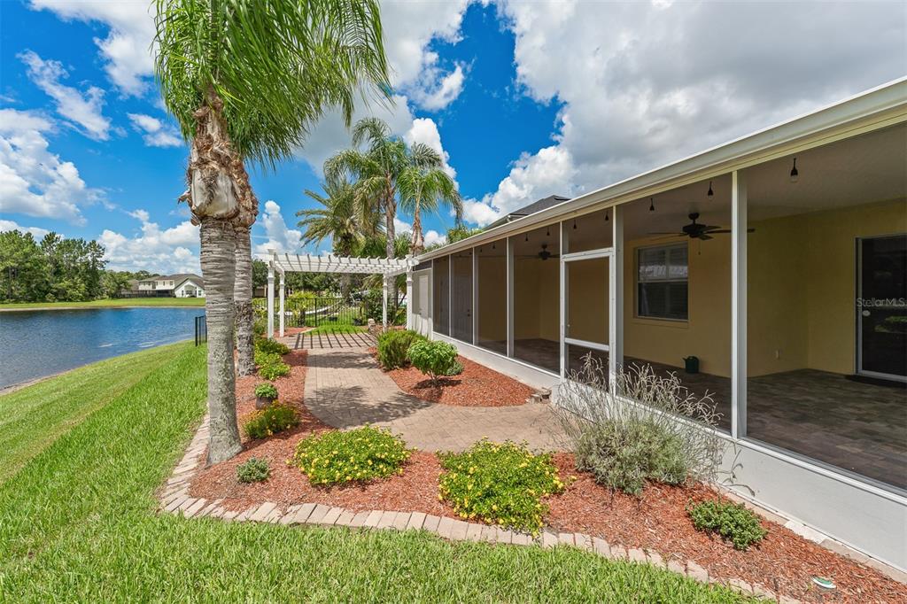 A screened-in patio overlooks a backyard with a pergola, landscaping, and a pond — 1465 BALSAM WILLOW TRAIL, ORLANDO, FL